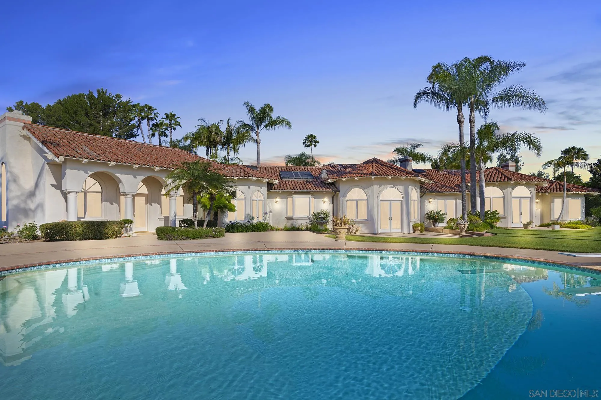 a view of a large pool with lawn chairs under an umbrella