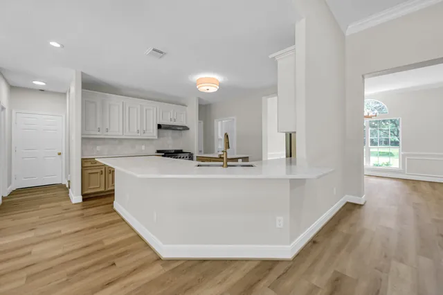 a large white kitchen with kitchen island a sink wooden floor and a refrigerator