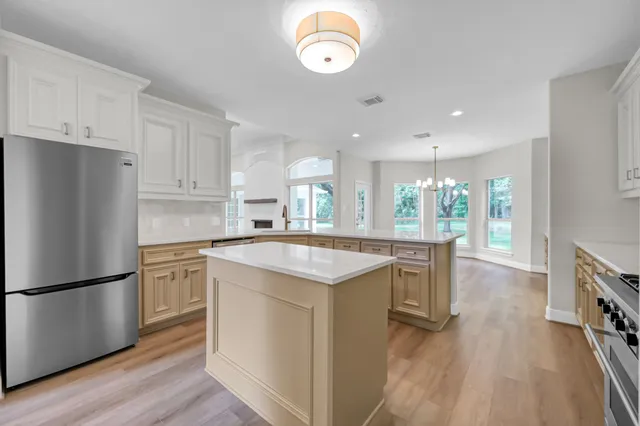 a kitchen with granite countertop a refrigerator a oven a stove and white cabinets with wooden floor