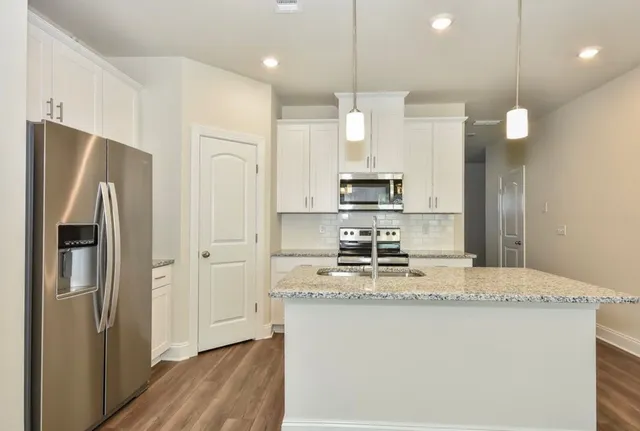 a kitchen with kitchen island granite countertop stainless steel appliances a refrigerator a stove cabinets dining table and chairs