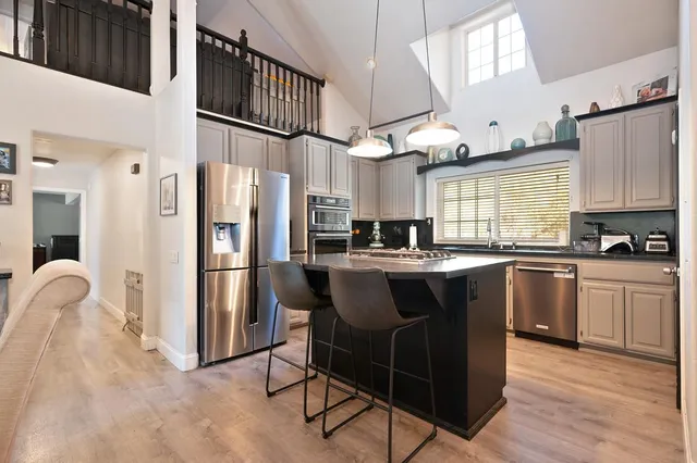 a kitchen with stainless steel appliances granite countertop a refrigerator a sink dishwasher a stove and a dining table with wooden floor