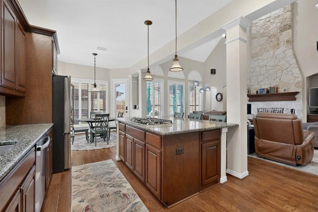 7625 Ridgedale Court Sachse, TX 75048 - Photo 11 of 40 Kitchen with a stone fireplace, dark wood-style floors, light stone counters, stainless steel appliances, and vaulted ceiling