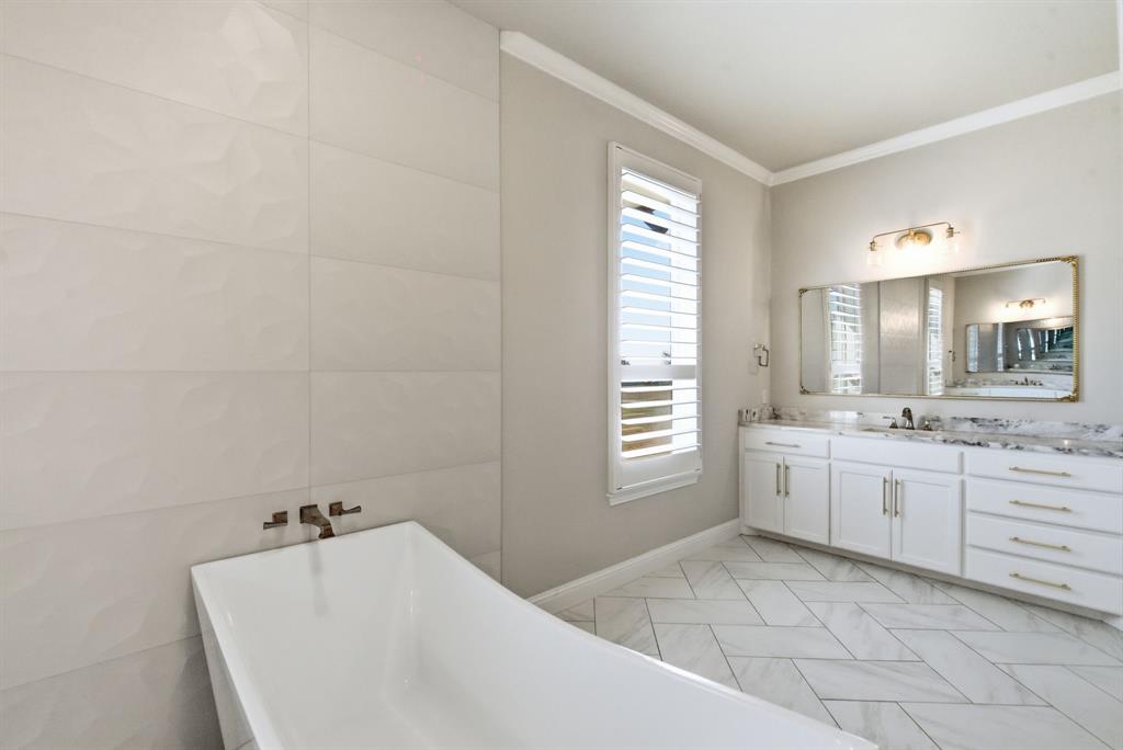 4600 Old Brock Road Weatherford, TX 76087 - Photo 24 of 37 Freestanding soaking tub with wall-mounted faucet, rectangular window with plantation shutters, double vanity with white cabinetry, marble-look countertop, and herringbone-pattern tile flooring