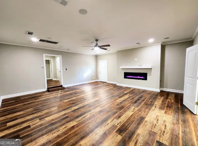 a view of empty room with wooden floor and kitchen view