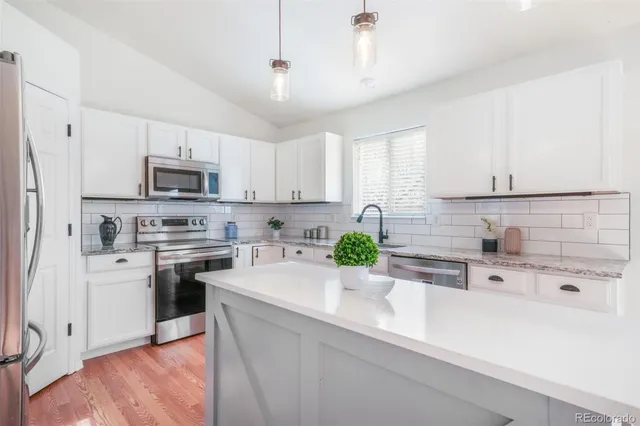 a kitchen with a sink a stove a microwave a refrigerator a white cabinets and wooden floor