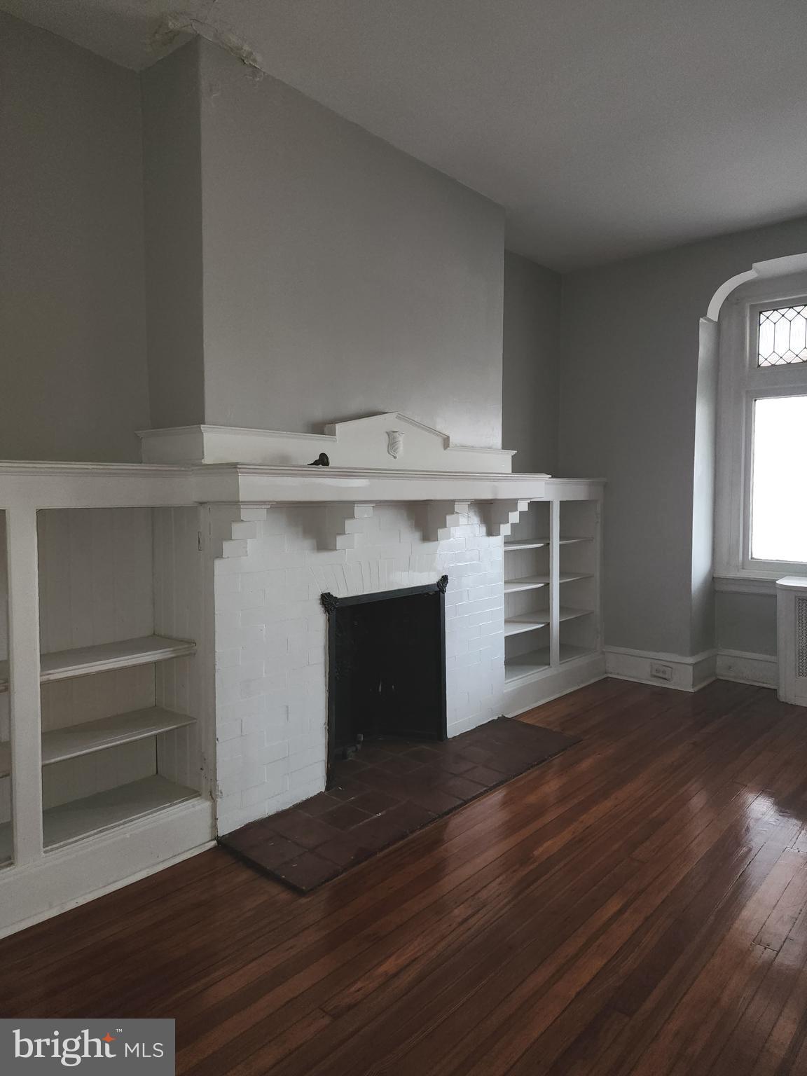 217 South 47th Street, Unit 2 Philadelphia, PA 19139 - Photo 7 of 22 an empty room with wooden floor a fireplace and windows