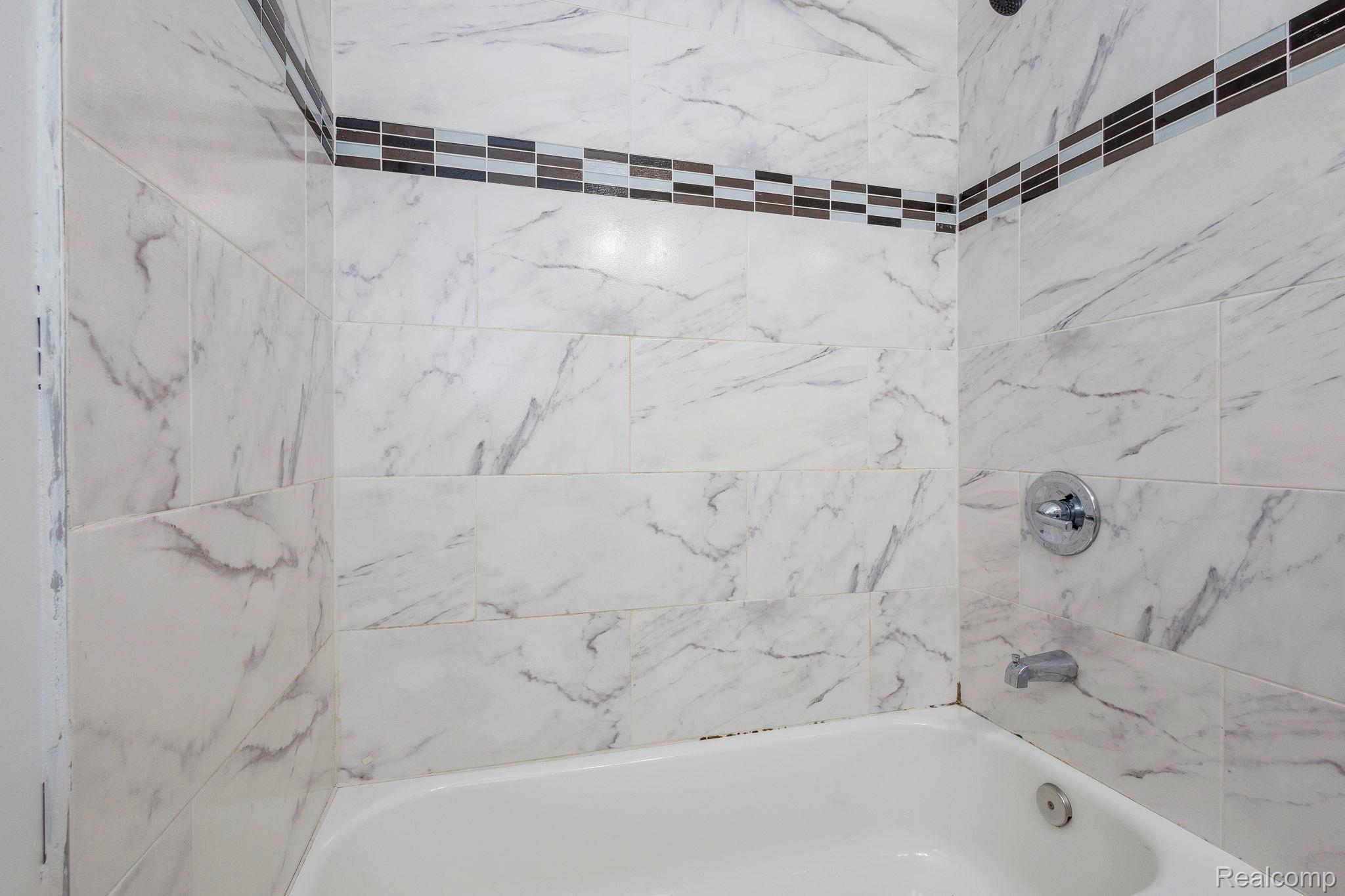 3974 Devonshire Road Detroit, MI 48224 - Photo 13 of 15 Bathtub with white subway tile surround featuring gray veining and a mosaic accent band