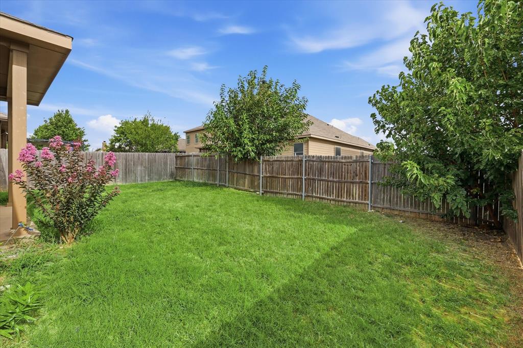720 Rio Bravo Drive Fort Worth, TX 76052 - Photo 32 of 38 Expansive backyard featuring a lush lawn, mature trees, a flowering shrub, and a wooden privacy fence