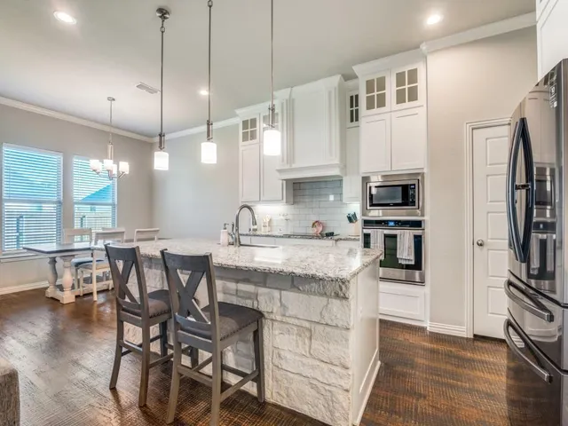 a kitchen with stainless steel appliances granite countertop a stove top oven a refrigerator a sink and white cabinets with wooden floor