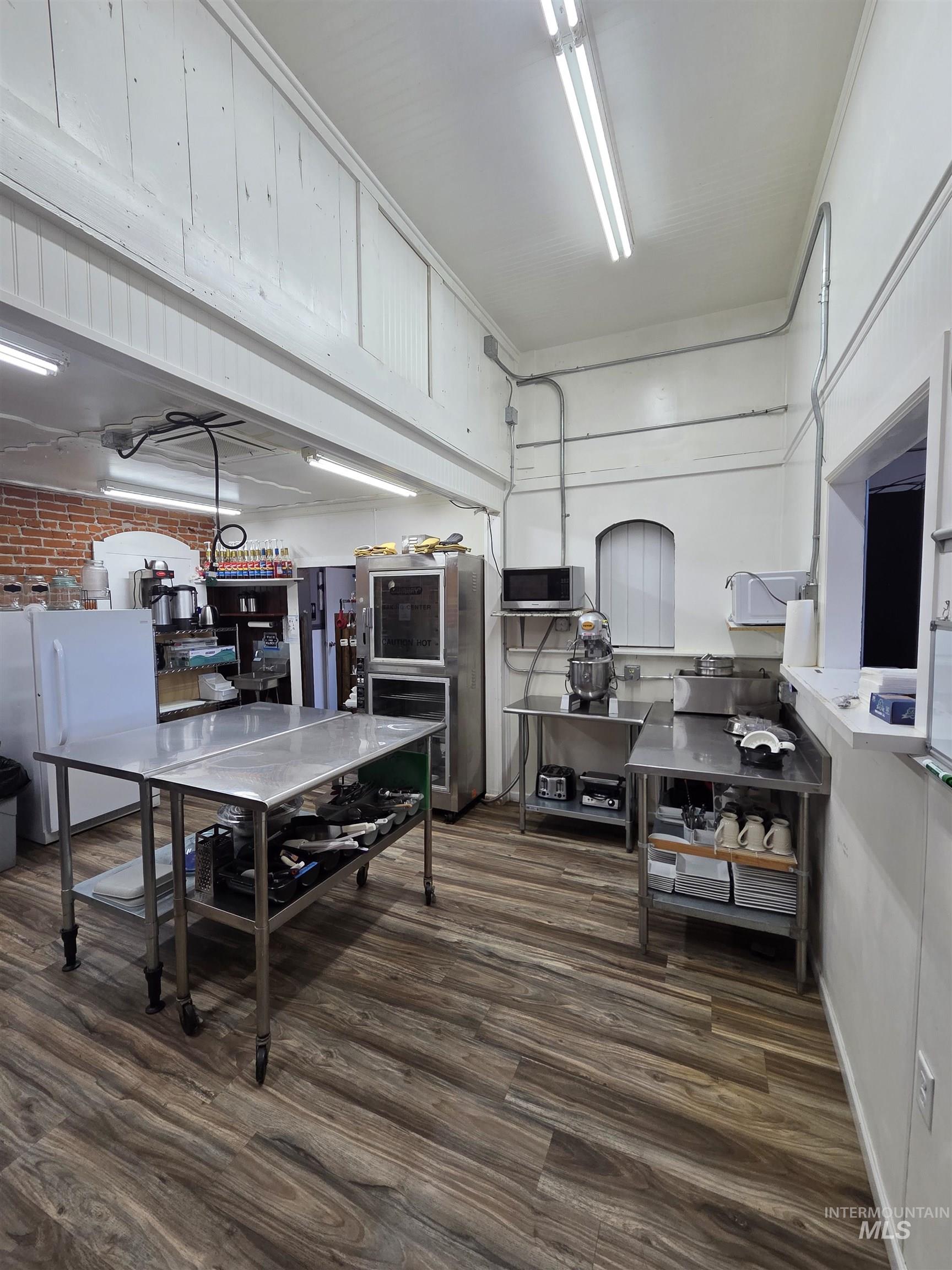 847 Main Street Pomeroy, WA 99347 - Photo 8 of 12 Spacious commercial kitchen featuring wood-finish flooring, ample stainless steel countertop and prep space, exposed brick accents, and abundant overhead fluorescent lighting