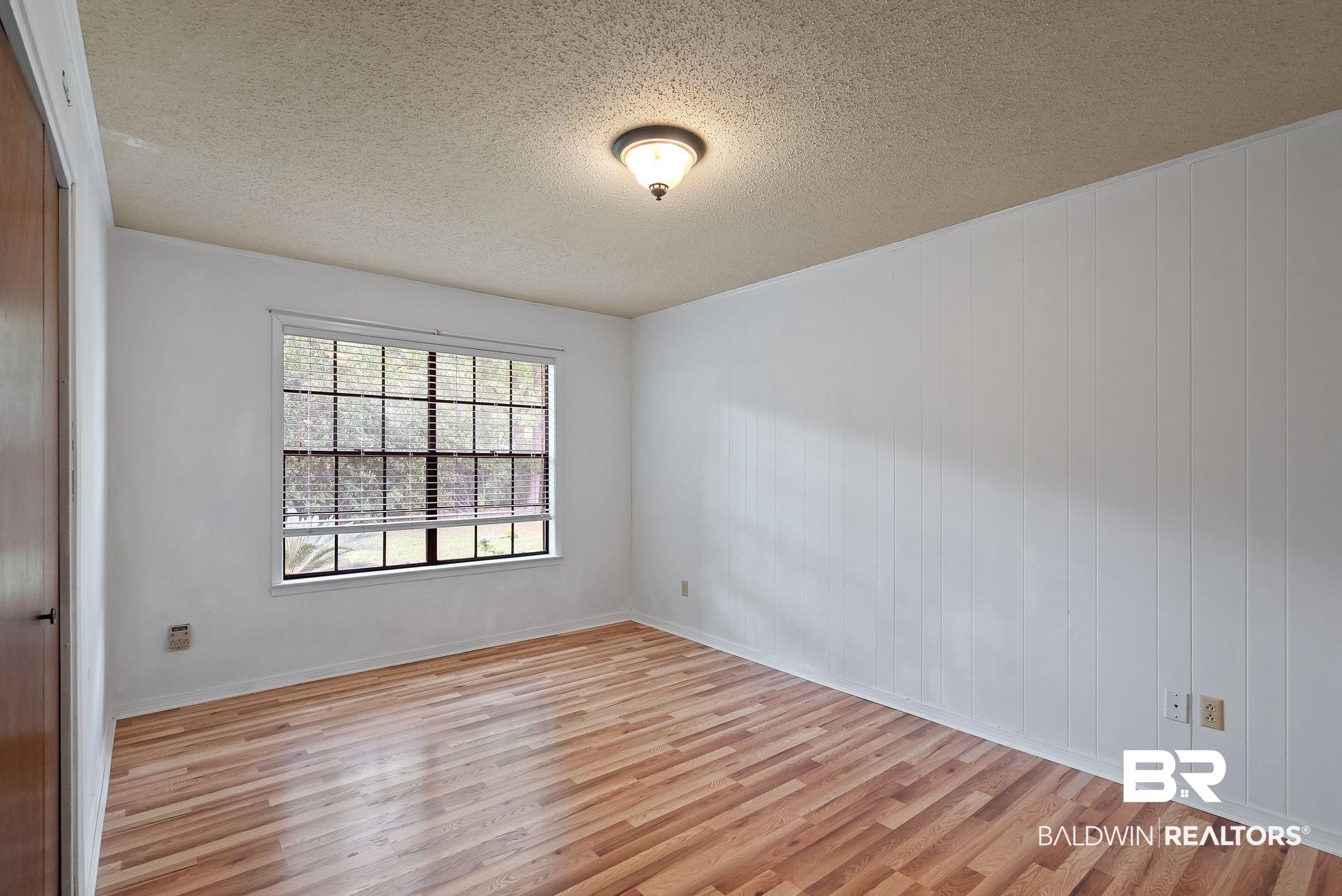 716 North Cedar Street Foley, AL 36535 - Photo 16 of 25 Light wood-finish flooring throughout, featuring a window with horizontal blinds, white paneled wall accents, a wood-finish door, and an overhead flush-mount light fixture