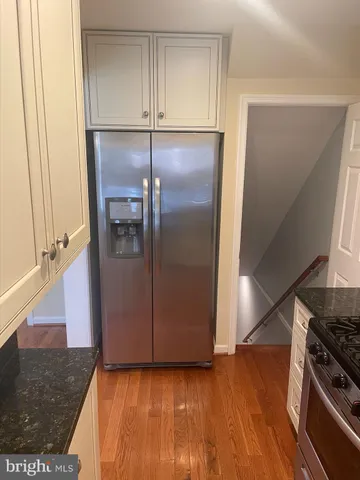 a view of a refrigerator in kitchen and an empty room with wooden floor