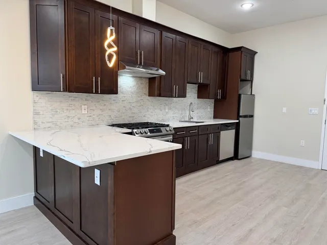 a kitchen with stainless steel appliances granite countertop a stove a refrigerator and a sink with wooden cabinets