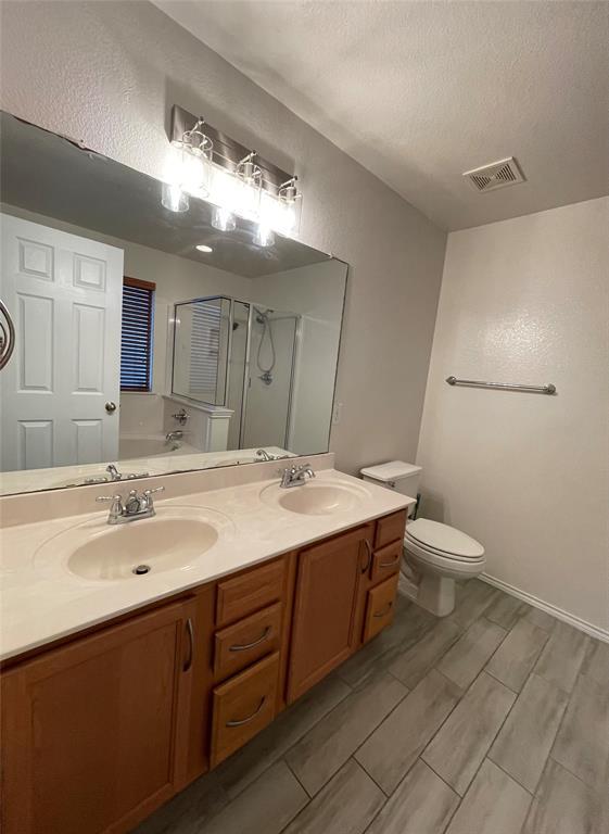 904 Watson Way Pflugerville, TX 78660 - Photo 11 of 16 Bathroom featuring double vanity, a bath, a shower stall, a textured wall, and wood finish floors