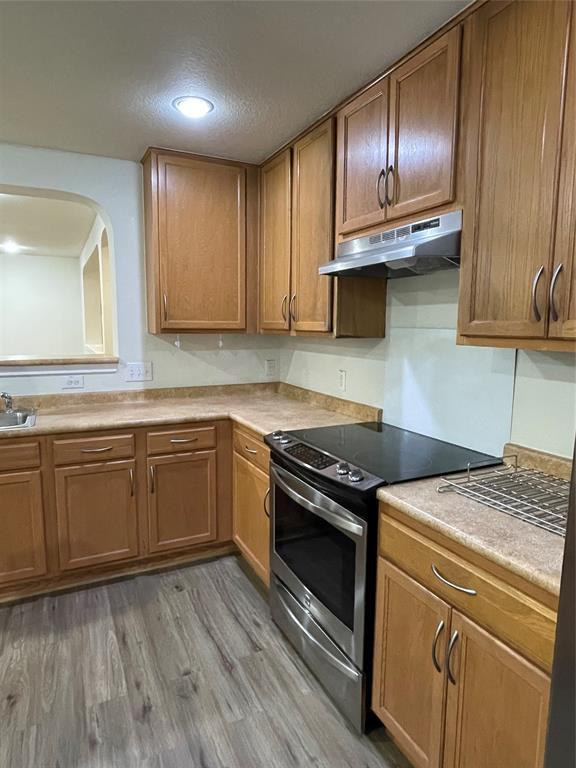 904 Watson Way Pflugerville, TX 78660 - Photo 7 of 16 Kitchen featuring stainless steel electric stove, brown cabinets, light countertops, under cabinet range hood, and dark wood-style floors