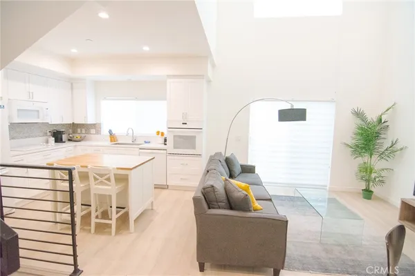 a living room with stainless steel appliances furniture a rug and a kitchen view