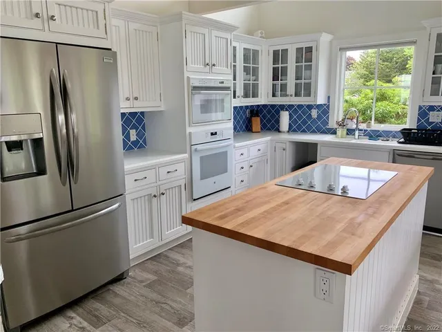 a kitchen with stainless steel appliances granite countertop a refrigerator a sink dishwasher a stove and white countertops with wooden floor