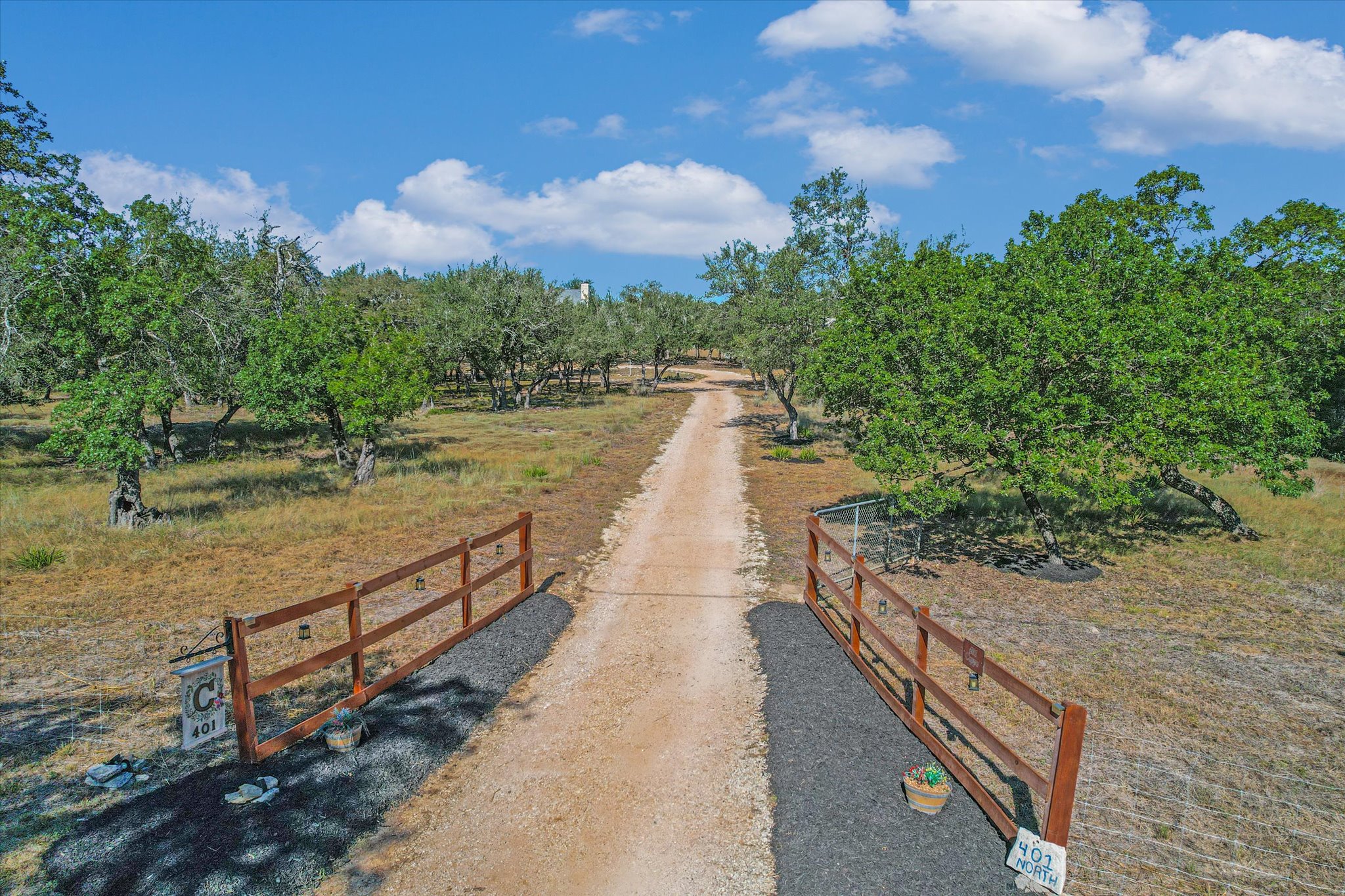 401 North Rainbow Ranch Road Wimberley, TX 78676 - Photo 36 of 39 Aerial view of the drive winds past mature oak trees and wooden fencing under a blue sky towards the main home.