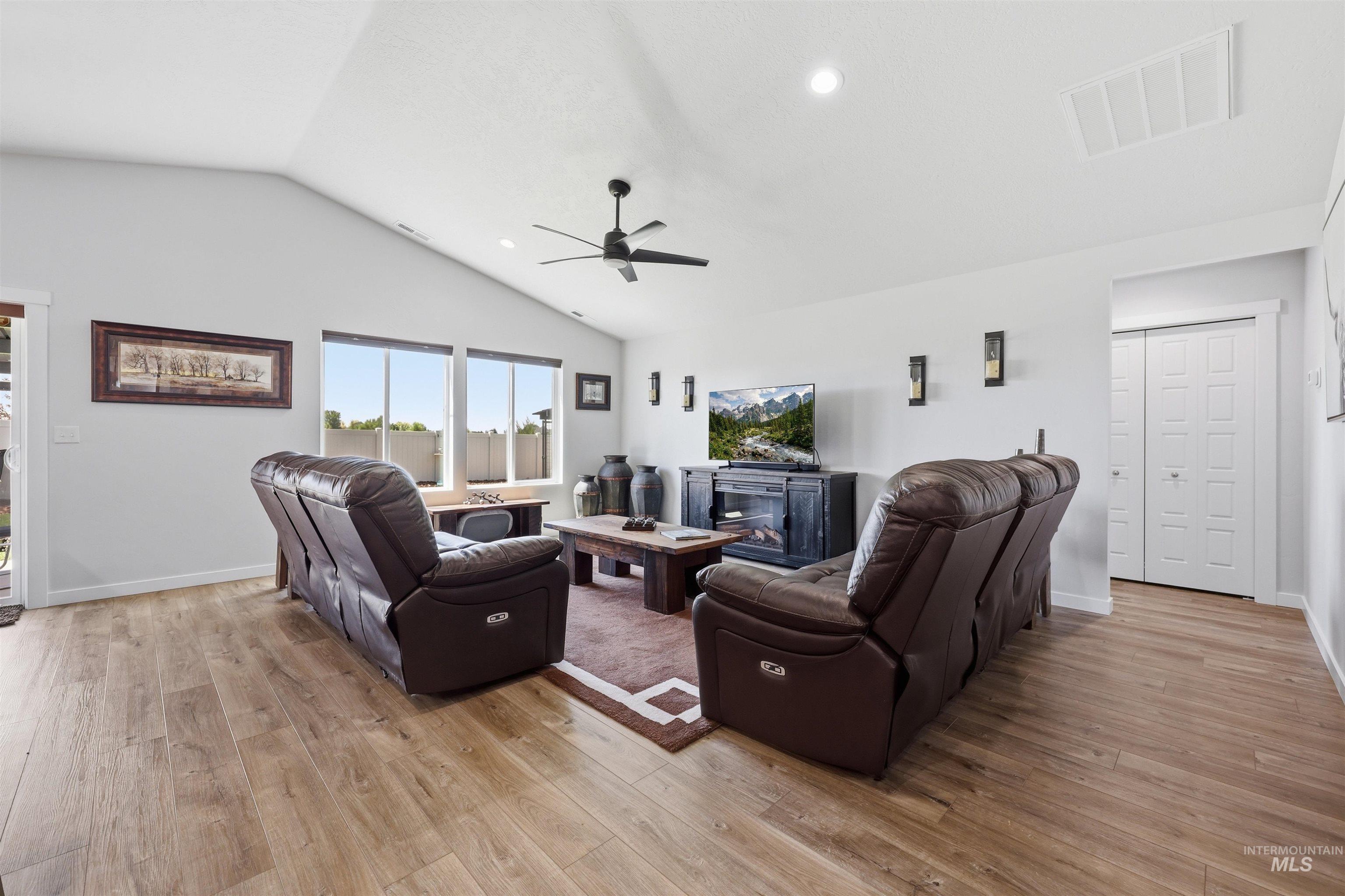 3811 West Maypearl Street Meridian, ID 83642 - Photo 12 of 39 Spacious living area featuring a vaulted ceiling with a ceiling fan, ample natural light from large windows, wood-finish flooring, recessed lighting, and a built-in electric fireplace media console