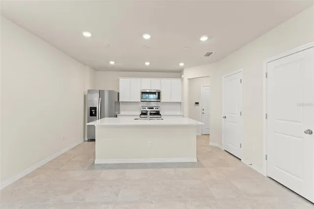 a view of kitchen with stainless steel appliances a refrigerator oven a white stove top oven with white cabinets