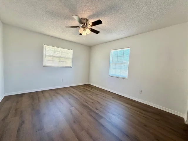 a view of an empty room with wooden floor and a fan