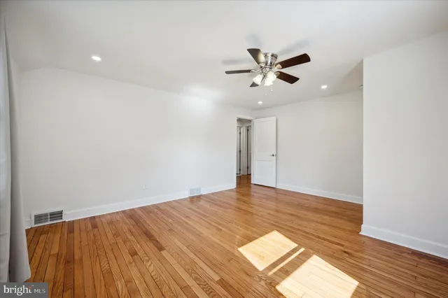 a view of an empty room with wooden floor and a ceiling fan