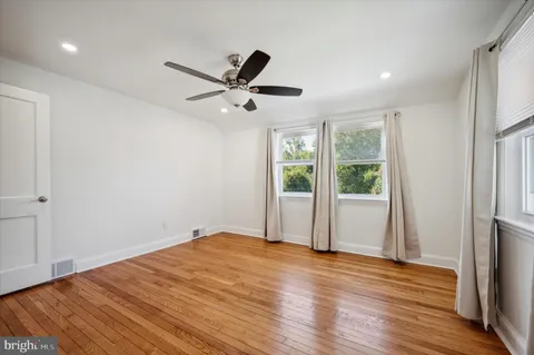 a view of an empty room with wooden floor and a ceiling fan