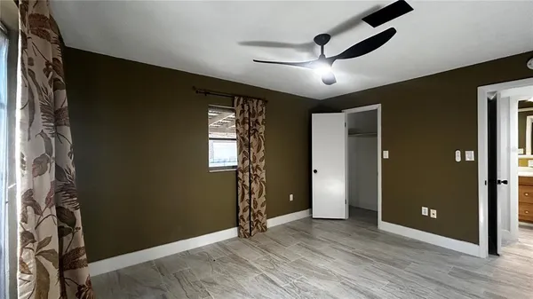 a view of an empty room with wooden floor and a ceiling fan