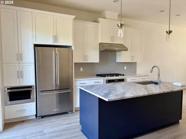 a kitchen with stainless steel appliances granite countertop a refrigerator a sink a stove and white cabinets with wooden floor