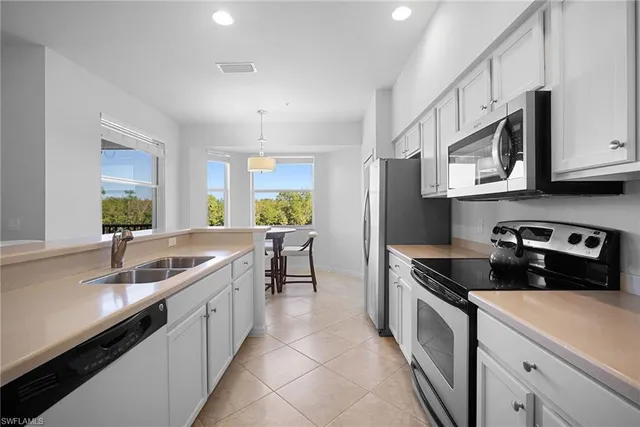 a kitchen with stainless steel appliances kitchen island granite countertop a dining table chairs and a refrigerator