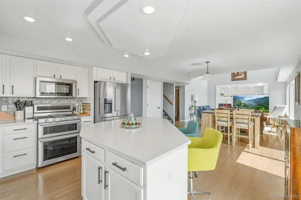 a kitchen with stainless steel appliances kitchen island granite countertop a refrigerator a stove top oven a sink dishwasher and white cabinets with wooden floor