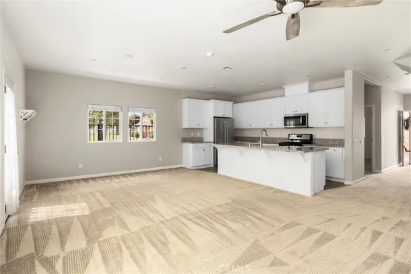 a living room with stainless steel appliances granite countertop a refrigerator a stove a sink dishwasher and white cabinets with wooden floor