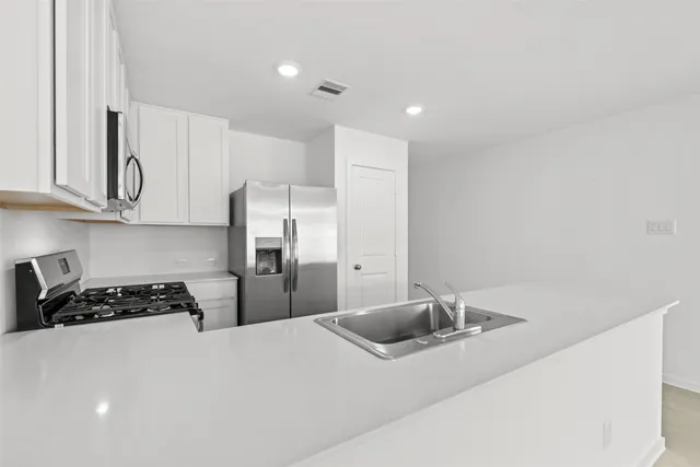 a kitchen with stainless steel appliances a refrigerator a sink a stove and white cabinets