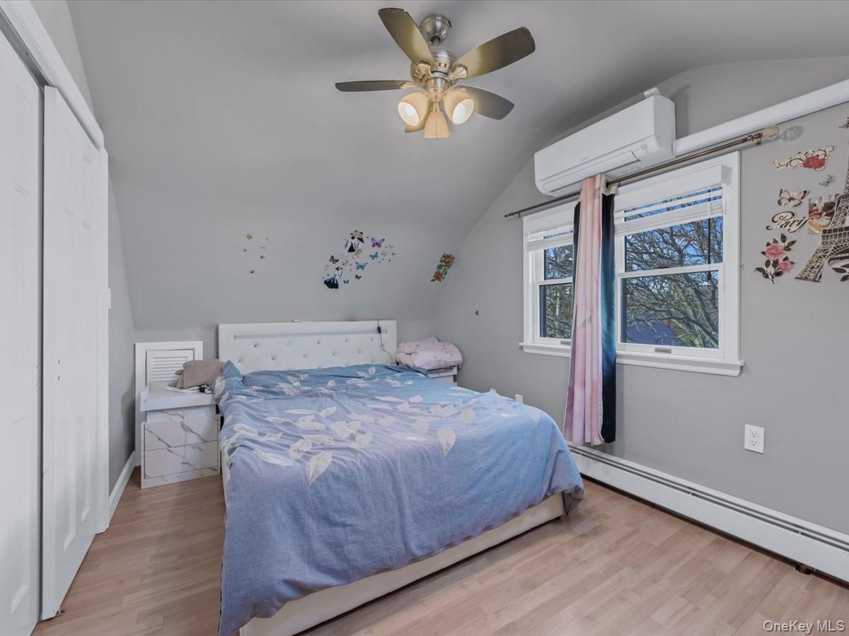 217-32 Corbett Road Queens, NY 11361 - Photo 19 of 25 Bedroom with vaulted ceiling, a wall mounted air conditioner, light wood-style flooring, a baseboard heating unit, and a ceiling fan