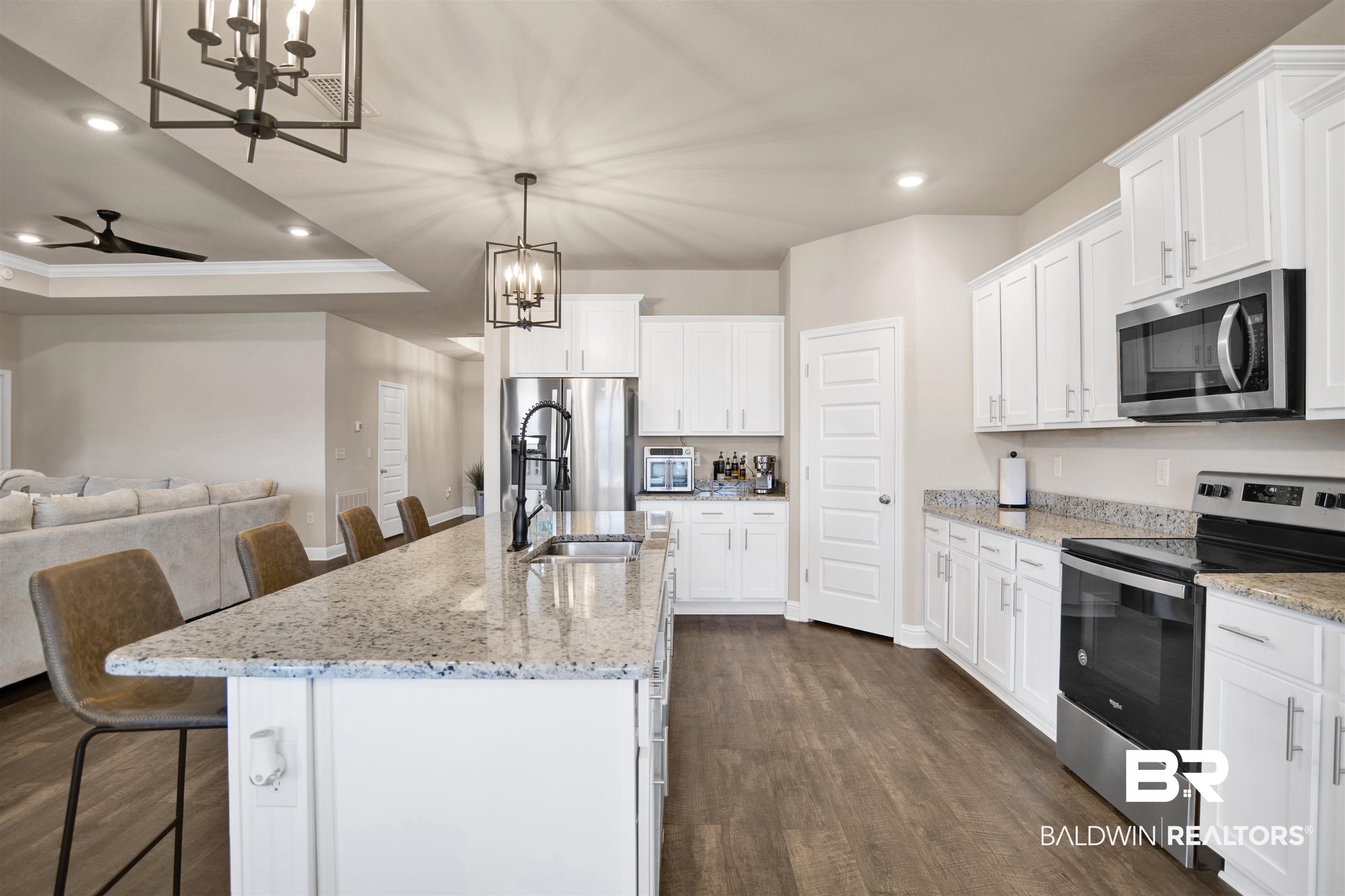 8493 Bronze Lane Foley, AL 36535 - Photo 13 of 38 Spacious kitchen featuring an expansive island with an undermount sink, ample white cabinetry, stainless steel appliances, and wood-finish flooring