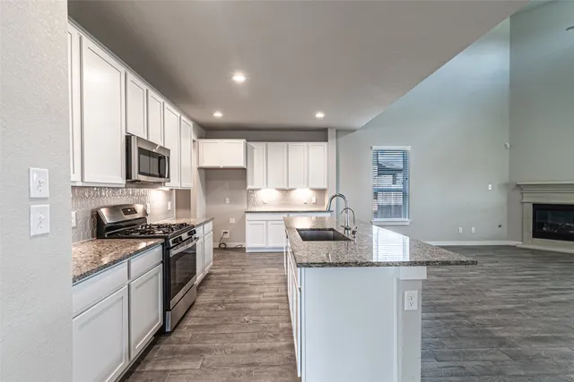 a kitchen with stainless steel appliances granite countertop a stove top oven a sink a refrigerator white cabinets and wooden floor