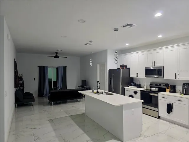 a large white kitchen with stainless steel appliances kitchen island a stove a refrigerator a sink dishwasher with a dining table and chairs