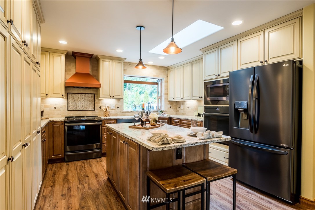 2707 187th Street Southeast Bothell, WA 98012 - Photo 6 of 39 a kitchen with a refrigerator a stove a sink dishwasher a oven with wooden floor and cabinets next to a window