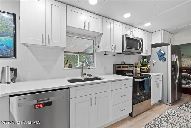 a kitchen with stainless steel appliances granite countertop white cabinets a sink a stove a refrigerator and microwave