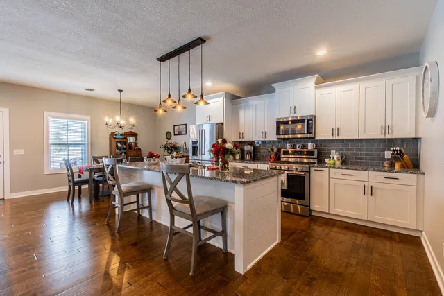 a kitchen with stainless steel appliances granite countertop a stove a sink a microwave a dining table and chairs