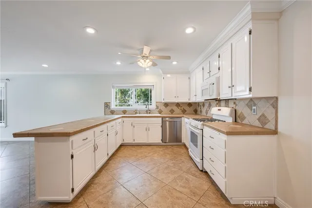 a large white kitchen with granite countertop a sink and dishwasher a stove top oven with white cabinets