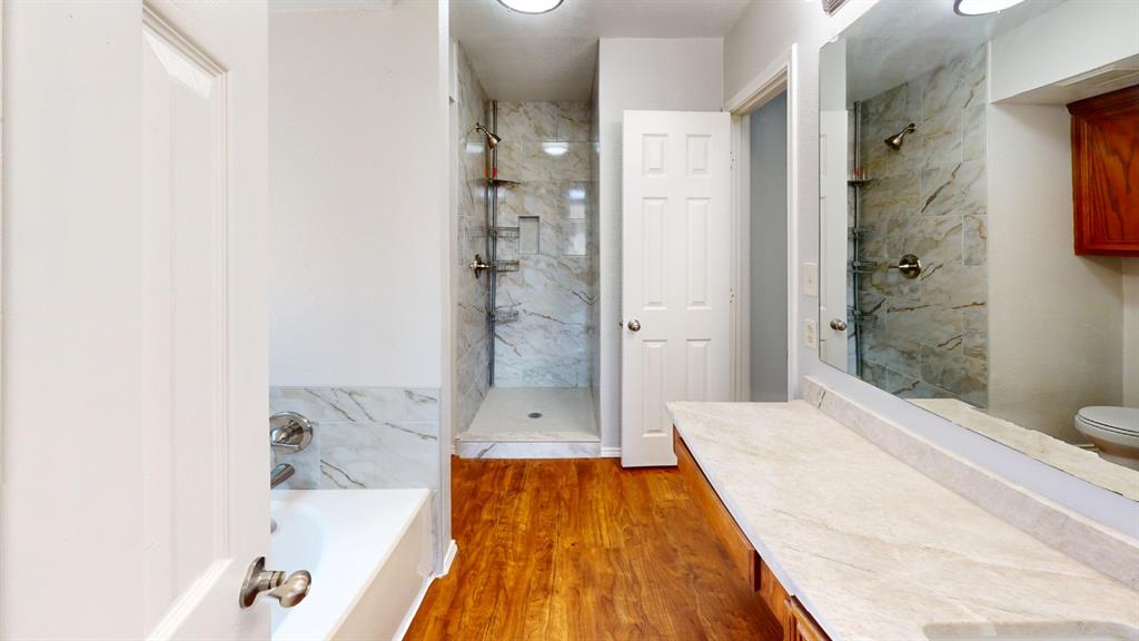 7913 Rice Drive Rowlett, TX 75088 - Photo 18 of 25 Bathroom featuring a dual vanity with a beige countertop, a large mirror, wood-finish flooring, a freestanding tub, and a separate shower with marble-look tile surround and built-in shelving