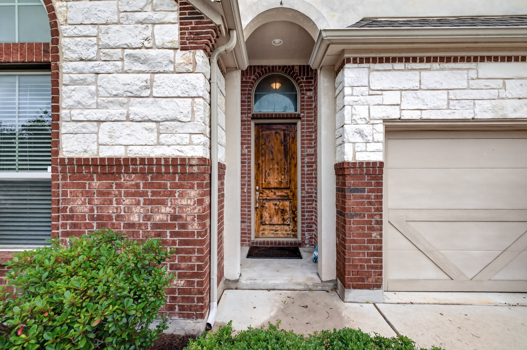 1017 Tabernash Leander, TX 78641 - Photo 4 of 38 Architectural facade featuring a distressed wood-paneled entry door with an arched transom window, set within a brick and stone exterior