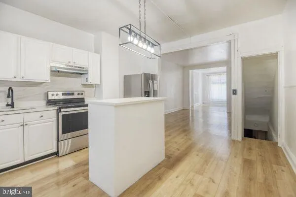 a kitchen with granite countertop a refrigerator oven a sink dishwasher and white cabinets with wooden floor