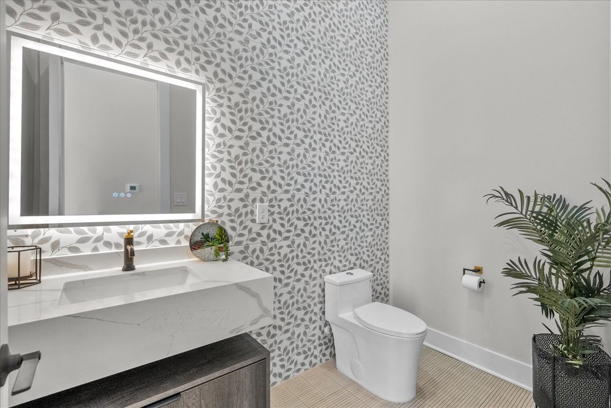 516 Reinerman Street Houston, TX 77007 - Photo 23 of 42 This bathroom features a stylish leaf-patterned accent wall, a modern vanity with a sleek illuminated mirror, and elegant fixtures. A potted plant adds a touch of greenery.
