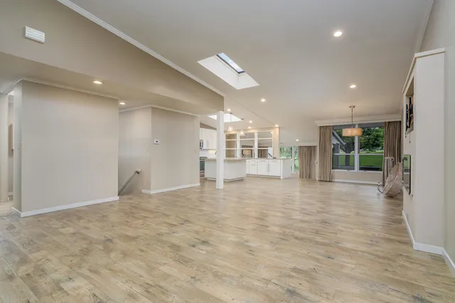 a view of an empty room with wooden floor and a kitchen