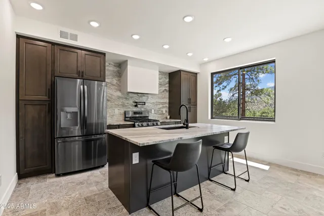 a kitchen with stainless steel appliances granite countertop a refrigerator a sink a stove a dining table and chairs