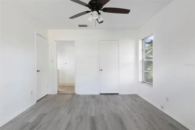 an empty room with wooden floor ceiling fan and windows