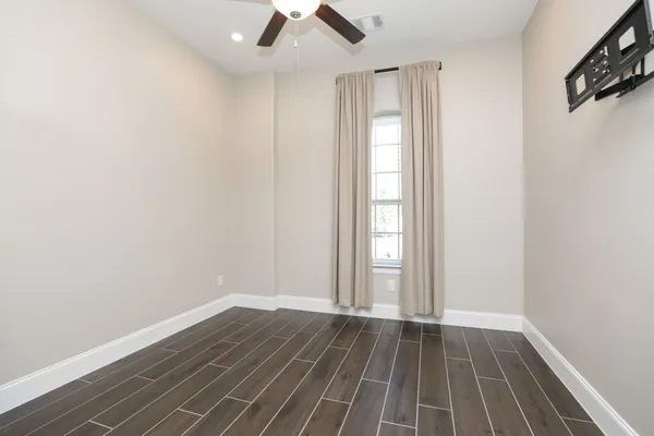 an empty room with wooden floor fan and windows