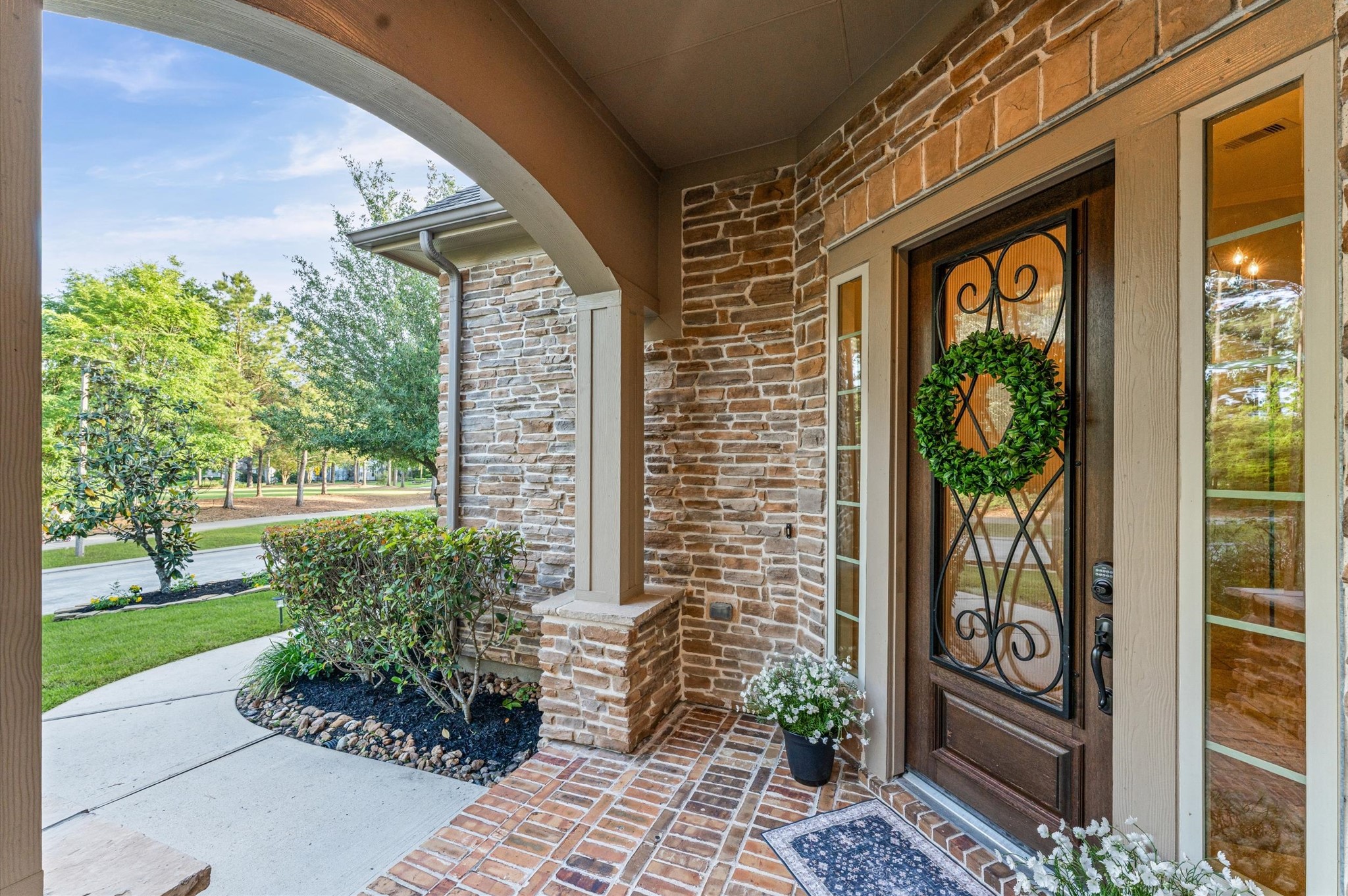 70 Valera Ridge Drive Spring, TX 77389 - Photo 8 of 37 Inviting front porch with decorative brickwork and stone accents, featuring an elegant front door with a wrought iron design and sidelights. The area is landscaped with greenery, offering a charming, welcoming entrance.